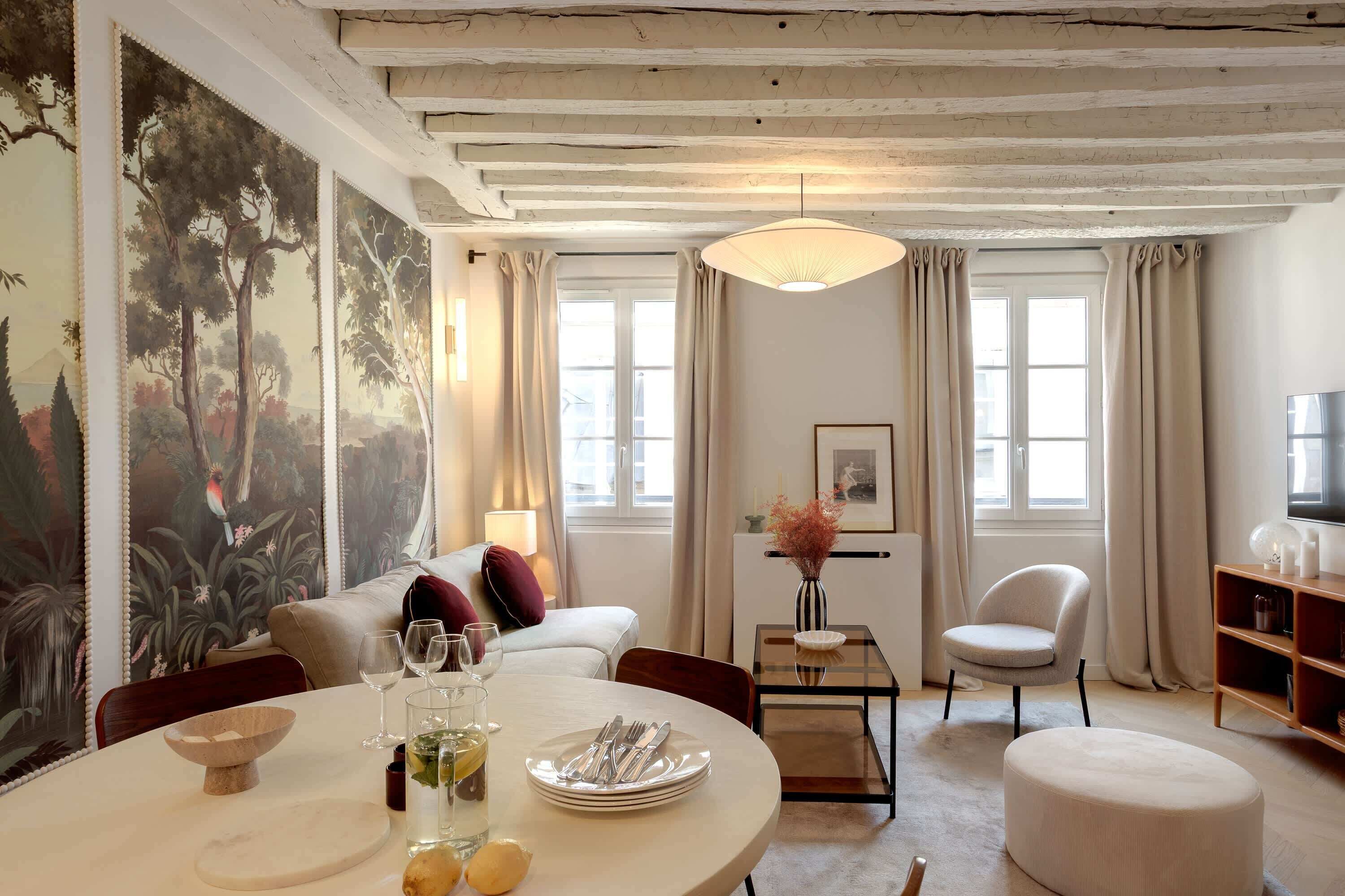 A well-lit room with a round dining table set for two, a sofa, a chair, and a television.