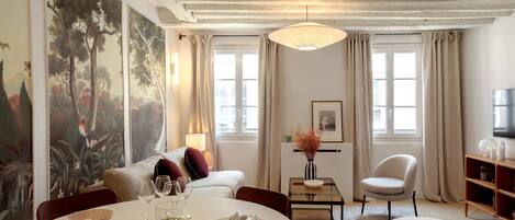 A well-lit room with a round dining table set for two, a sofa, a chair, and a television.