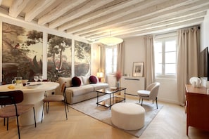 Ein modernes Wohnzimmer mit einer Couch, einem Couchtisch und Sesseln, ein Essbereich mit Tisch und Stühlen sowie ein großes Bild an der Wand.
