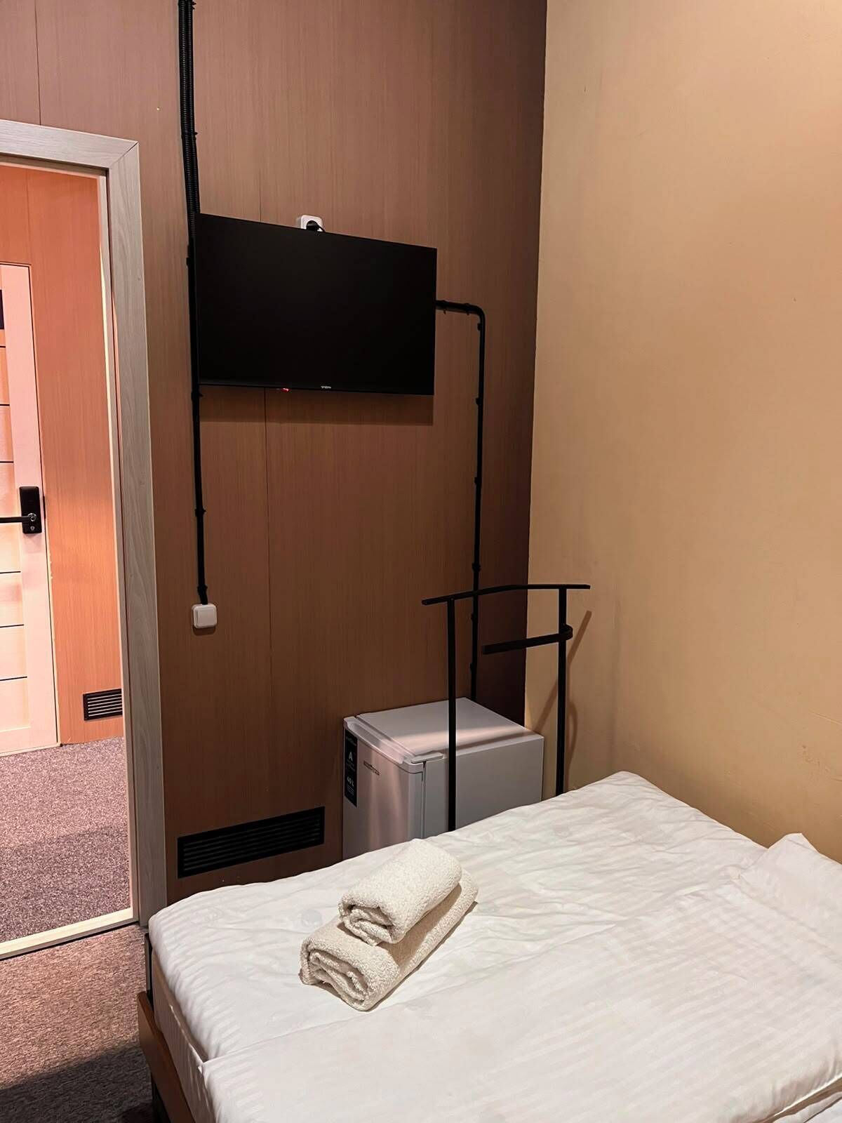 A hotel room with a bed, a television mounted on the wall, and a small refrigerator.