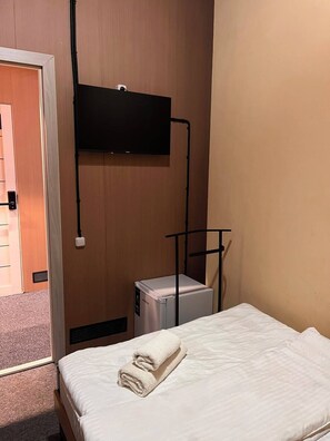 Habitació d'hotel amb un llit, una televisió penjada a la paret i un frigorífic petit.