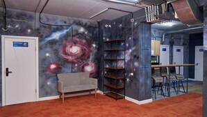 A room with a galaxy-themed mural, a sofa, a wooden bookshelf, and a door labeled 'NEPTUNE.' - Gagarin Capsule Hotel  (Almaty)