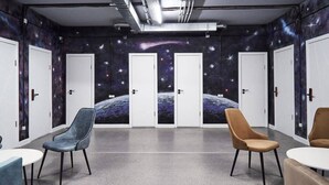 A room with a space-themed mural, four white doors, and two round tables with chairs. - Gagarin Capsule Hotel  (Almaty)