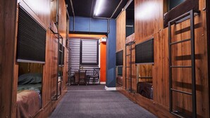 A narrow hallway with wooden walls, a central table with chairs, and a bed on the left. - Gagarin Capsule Hotel  (Almaty)