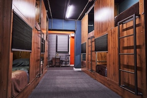 A narrow hallway with wooden walls, a central table with chairs, and a bed on the left.