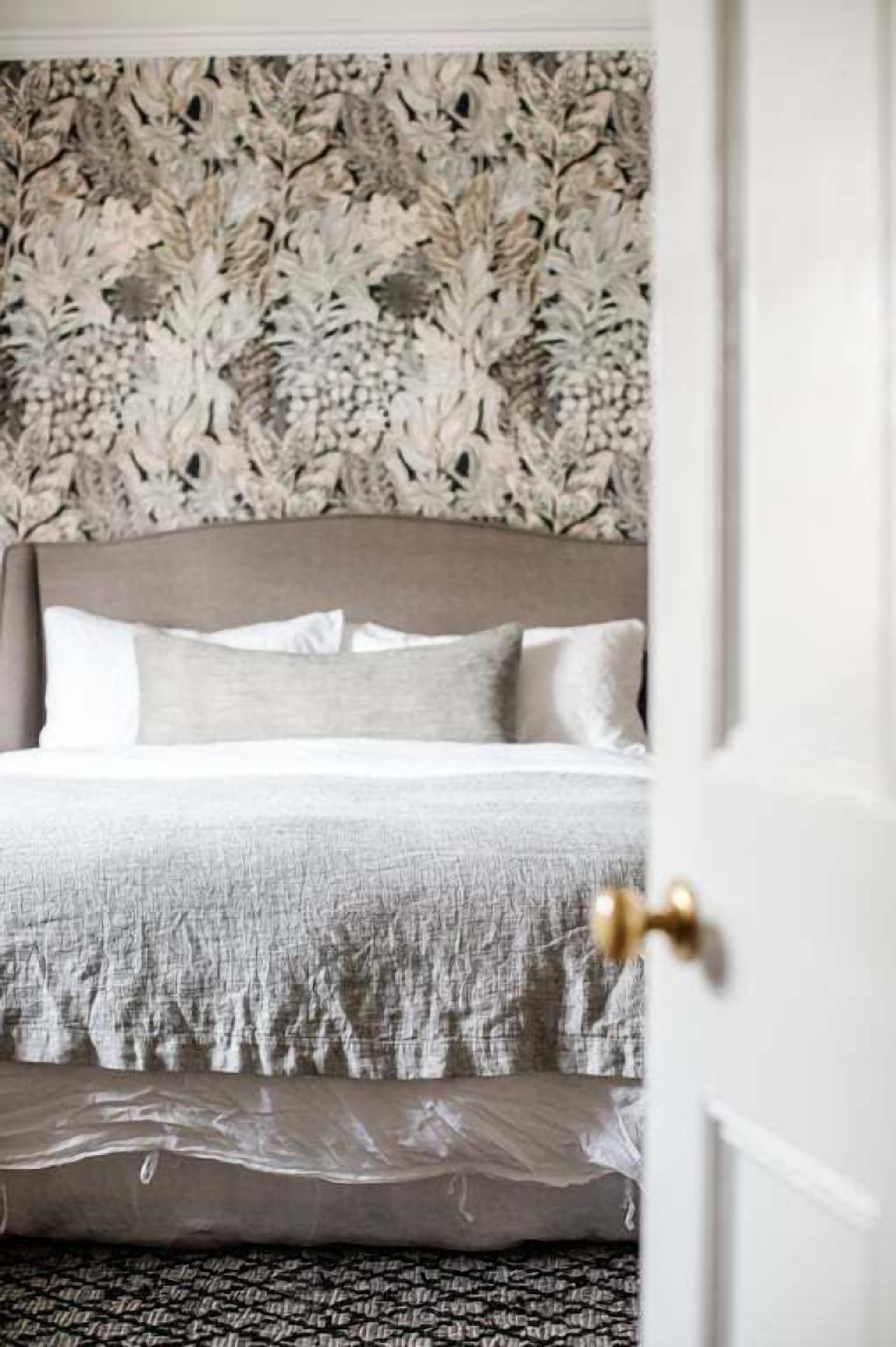 A bedroom with a patterned wallpaper, a bed with a grey headboard, and a patterned rug.