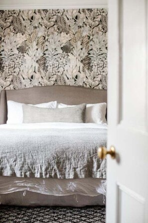 A bedroom with a patterned wallpaper, a bed with a grey headboard, and a patterned rug.
