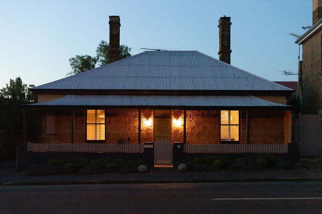 A two-story building with a metal roof, two chimneys, and a front porch with a white picket fence.