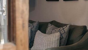 Un salón con un sofá verde, una mesita de madera y dos cuadros en la pared.
