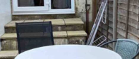 Un patio con una mesa redonda y cuatro sillas, una puerta corrediza de vidrio y una valla de madera.