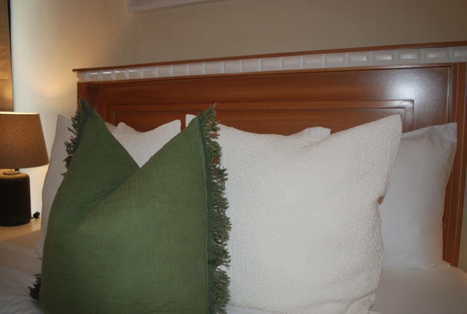 A bed with white pillows and a green pillow, a wooden headboard, and a bedside lamp.