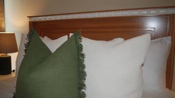 A bed with white pillows and a green pillow, a wooden headboard, and a bedside lamp.