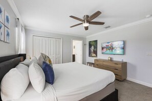 Ein Schlafzimmer mit einem Bett, Deckenventilator, Kommode, Fernseher und Bildern an den Wänden.