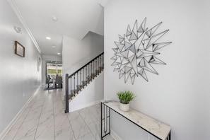 Ein Flur mit Treppe, Marmorboden und einem geometrischen Kunstwerk an der Wand.