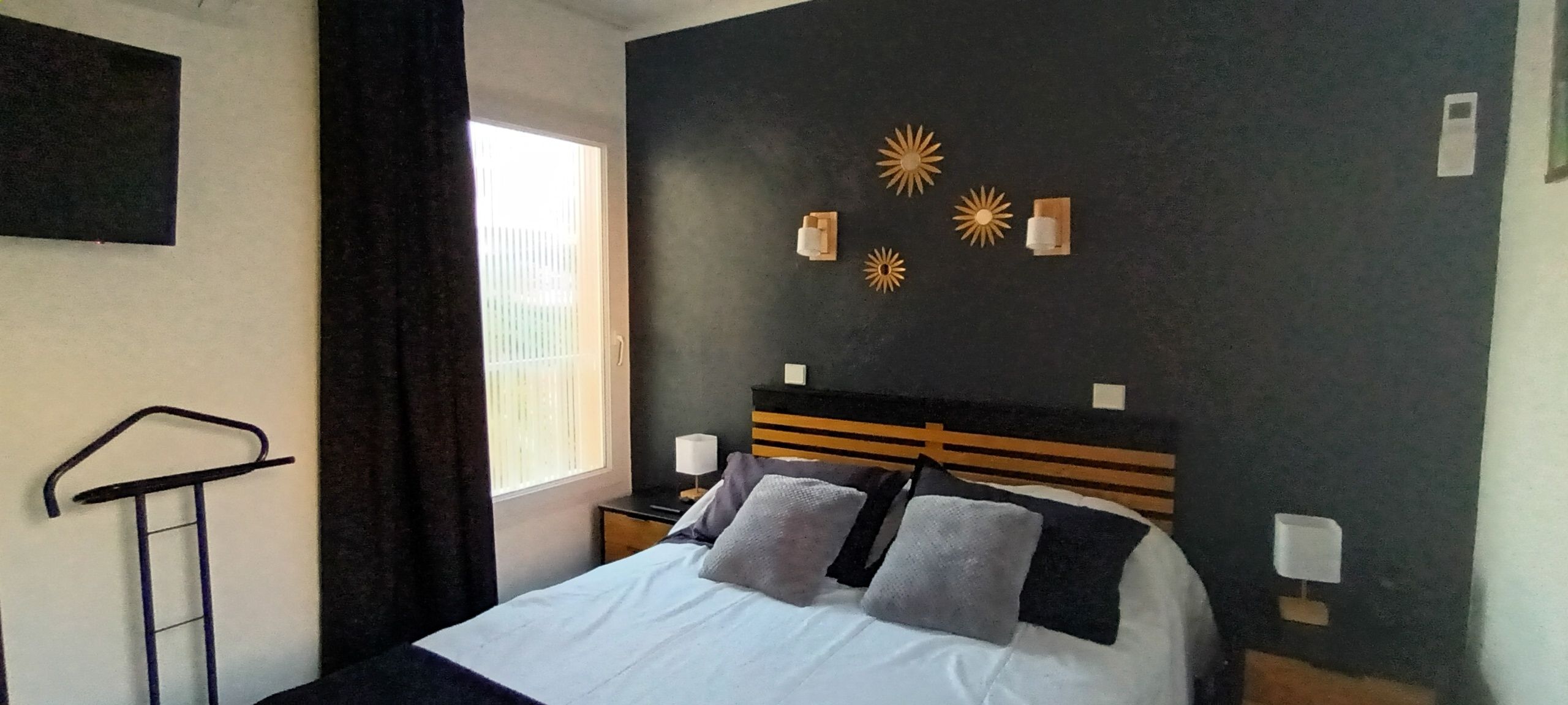 A bedroom with a bed, a nightstand, a wall-mounted lamp, and a window with curtains.