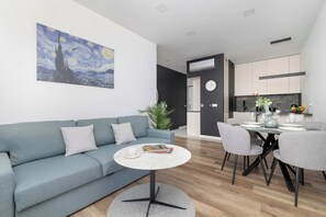 A modern living room with a blue sofa, a round coffee table, and a painting of a night sky. - Stylish Apartment | Underground Parking | Close to Spodek Arena (Katowice)