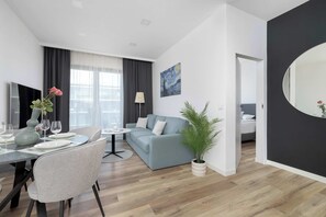A modern living room with a dining area, a sofa, a coffee table, and a potted plant. - Stylish Apartment | Underground Parking | Close to Spodek Arena (Katowice)