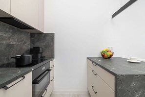 A modern kitchen with a black countertop, a pot on the stove, and a fruit bowl on the counter. - Stylish Apartment | Underground Parking | Close to Spodek Arena (Katowice)