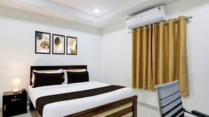 Una habitación de hotel con cama, mesita de noche, una silla y aire acondicionado instalado en la pared.