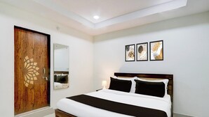 Un dormitorio con puerta de madera, cama con ropa de cama blanca y negra, mesita de noche con lámpara y tres cuadros en la pared.