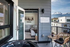 Un appartement moderne doté d’un balcon, d’un canapé, d’un fauteuil en osier et d’un espace avec jacuzzi.