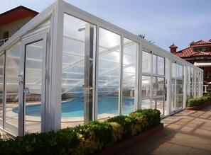 Ein von Glas umschlossener Poolbereich mit freiem Blick auf das Schwimmbecken und die umliegende Bepflanzung.