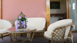 Een kamer met een glazen tafel, rieten stoelen, een witte bank en een wandlamp.