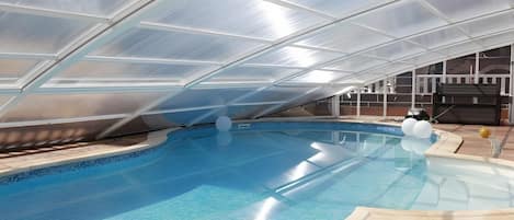 Una piscina interior con techo de cristal, agua cristalina y un área de descanso con vistas a la piscina.