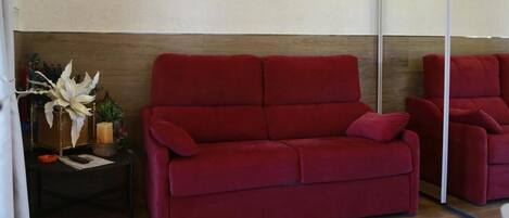 Un sofá rojo en una habitación con vigas de madera en el techo y un espejo grande en la pared.