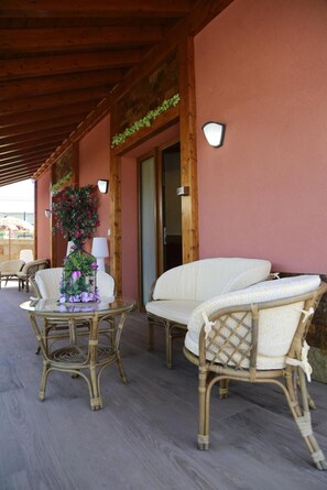 An outdoor seating area with wicker furniture and a glass table, under a wooden pergola with a pink wall. - Studio with Terrace and Pool (Miengo)