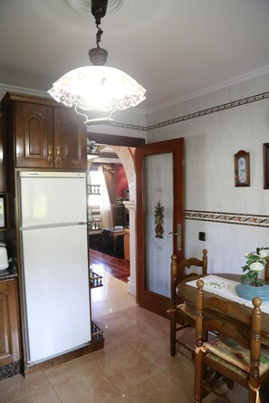 Eine Küche mit Holzschränken, einem weißen Kühlschrank, einem Esstisch mit Stühlen und einer Kandelaber.