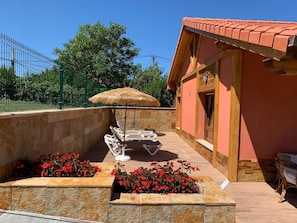 A sunlit outdoor area with a pool, lounge chairs, a thatched umbrella, and red flowers. - Casa La Arena with pool (Miengo)