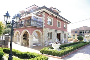 A two-story building with a balcony, arched entrance, and a garden with a fountain. - Casa La Arena with pool (Miengo)