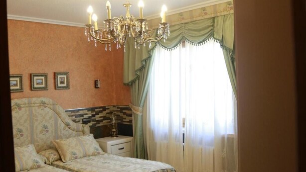 A bedroom with a large bed, a nightstand, a lamp, a chandelier, and a window with curtains. - Casa La Arena with Pool (Miengo)