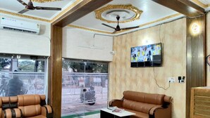 A modern living room with a sofa, a coffee table, a television mounted on the wall, and a ceiling fan. - Hotel Ashirwad And Marriage Hall (Deoghar)