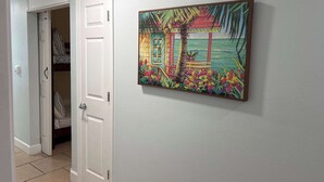 Een hal met een deur die leidt naar een kamer met een bed en een inloopkast. Op de muur hangt een schilderij van een tropisch landschap.