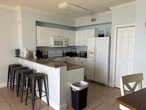 A kitchen with white cabinets, a microwave, a stove, a refrigerator, and a trash bin. - Gulf Front Condo with Pool, Hot Tub & Beach Access (Panama City Beach)