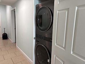 A laundry room with two front-loading washing machines, a tiled floor, and a door leading to another room. - Gulf Front Condo with Pool, Hot Tub & Beach Access (Panama City Beach)