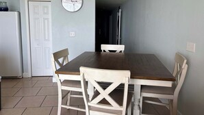 Een eethoek met een houten tafel, witte stoelen en een wandklok.
