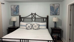 Een slaapkamer met een bed, twee nachtkastjes, twee wandlampen, een plafondventilator en twee ingelijste kunstwerken aan de muur.