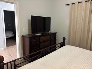 A bedroom with a bed, a dresser with a television on top, and a door leading to another room. - Gulf Front Condo with Pool, Hot Tub & Beach Access (Panama City Beach)