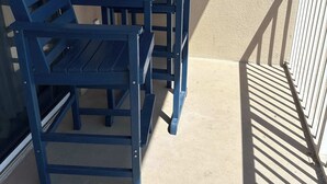 Een balkon met een tafel, stoelen, een leuning en uitzicht op de buitenkant van het gebouw.