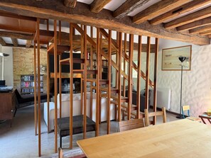 A room with exposed wooden beams, a staircase, a bookshelf, a radiator, and a framed picture on the wall. - La Grange du Vaudoué (Le Vaudoué)