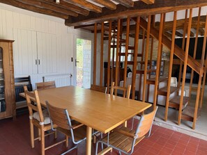 A dining area with a wooden table and chairs, a white door, and a staircase. - La Grange du Vaudoué (Le Vaudoué)