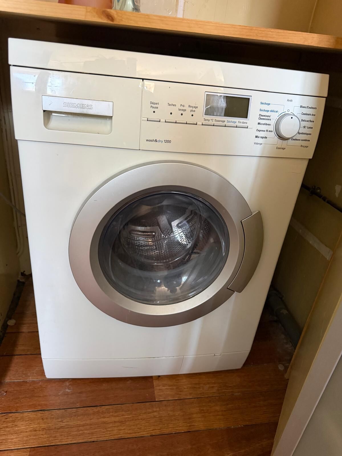 A white Siemens washing machine with a control panel, located in a room with wooden flooring.
