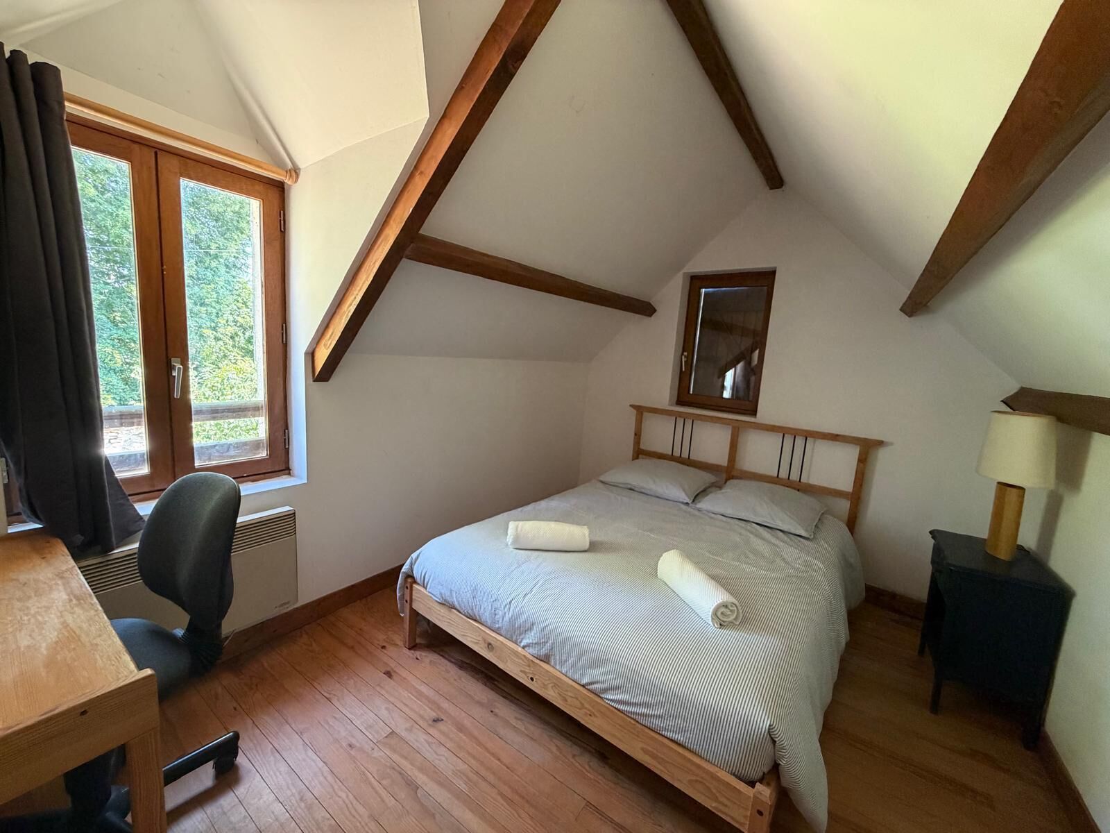 Une chambre avec un plafond en pente, un lit en bois, un bureau et une chaise.