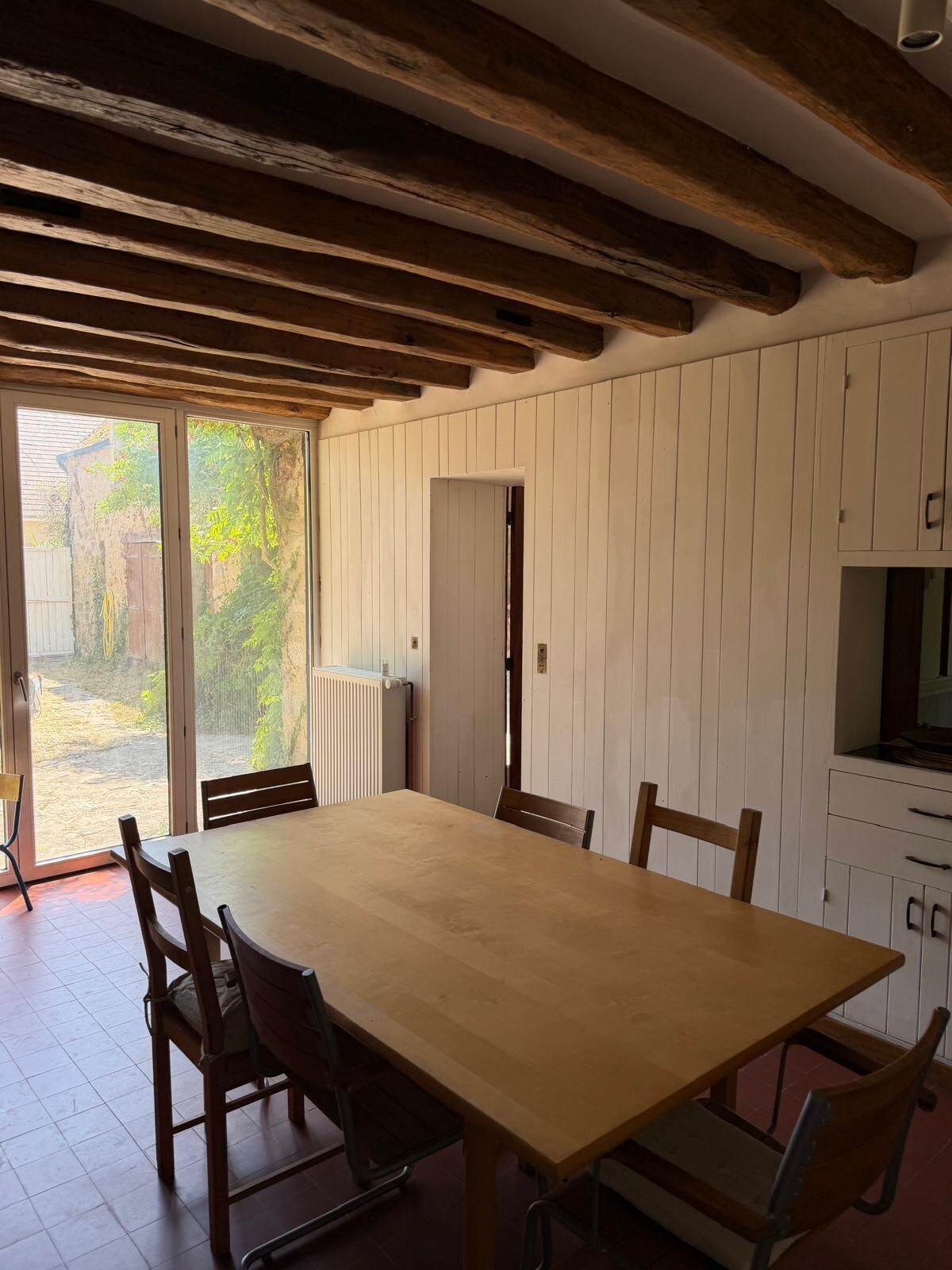 A dining area with a wooden table and chairs, a sliding glass door to the outside, and white wooden cabinets.
