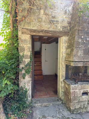 Ein steiner Torbogen führt in einen Raum mit einer Holztreppe und einem Fliesenboden.