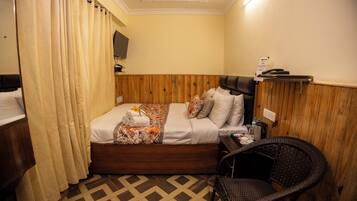 A hotel room with a wooden headboard, a bed with a floral bedspread, a wicker chair, and a small table with toiletries.