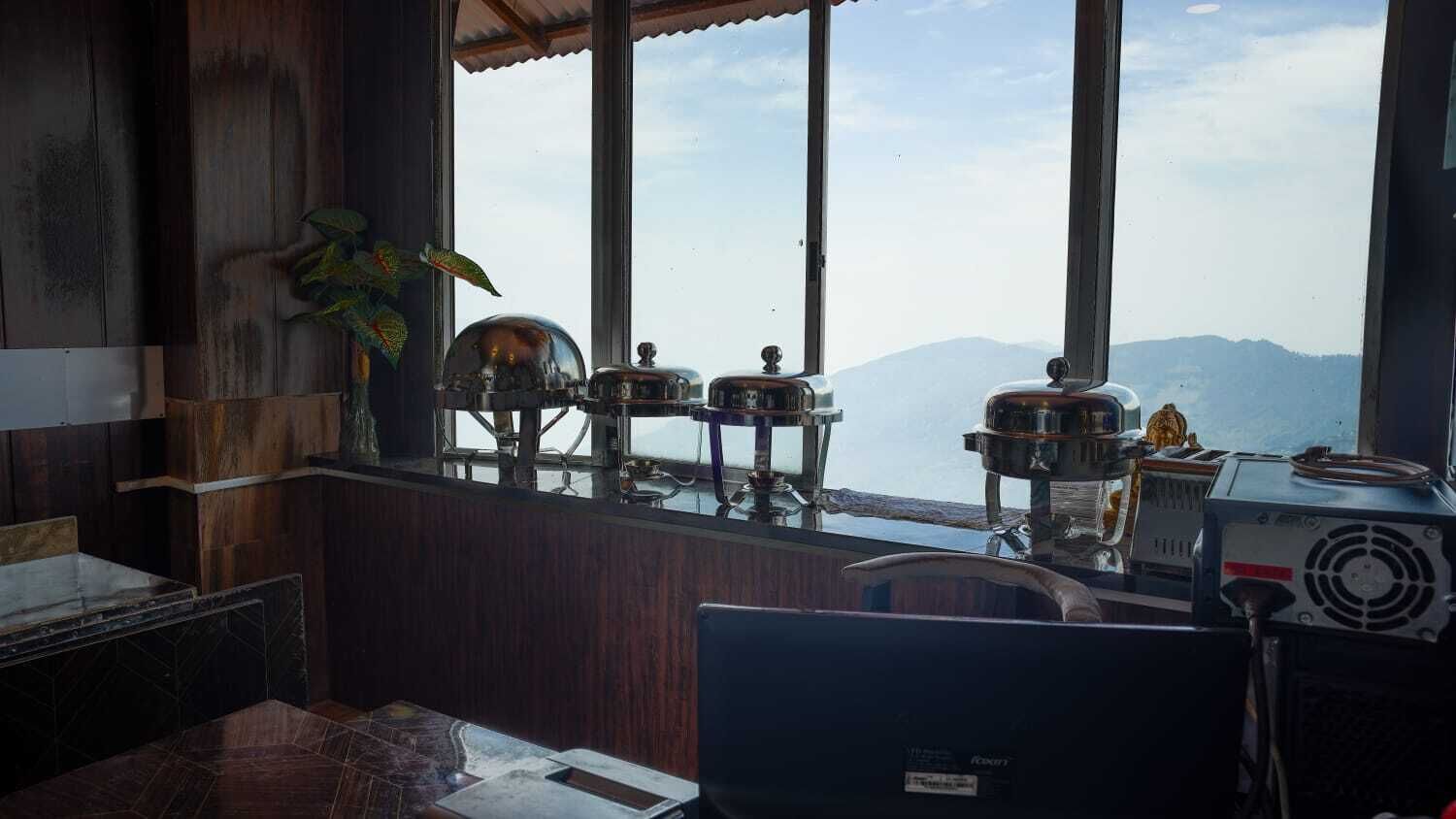 Una habitación con vistas a montañas a través de amplios ventanales, interior de madera y un escritorio con ordenador.